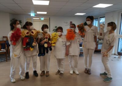 Betreuungskräfte stehen mit Handpuppen in einer Reihe. Alle haben Masken auf.