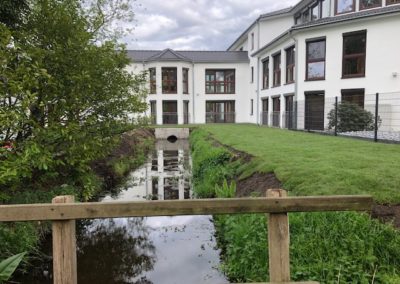 Aufnahme des Grabens der unter dem Haus durchläuft und grünem Rasen.